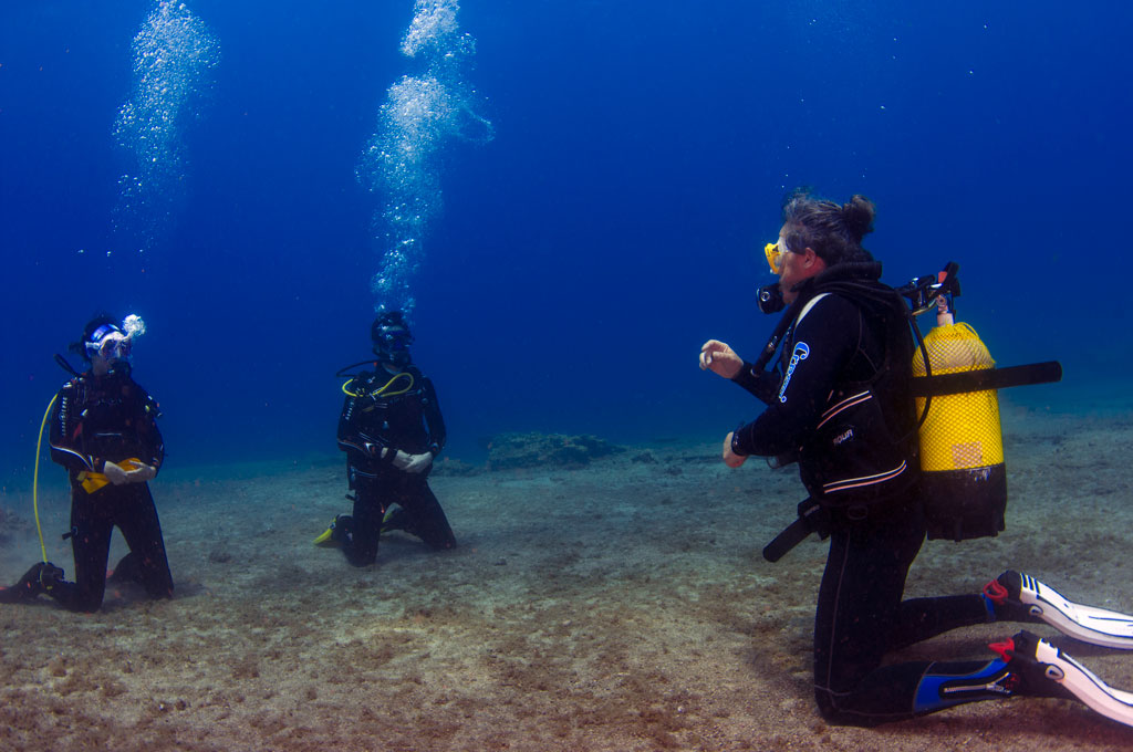 Instructor y dos alumnos de rodillas en el fondo en un curso de buceo en Tenerife Sur Las Galletas